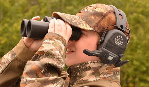 Kid looking through binoculars while wearing Walkers hearing protection